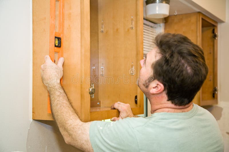 Carpenter installing solid maple kitchen cabinets, using a level to check his work. Carpenter installing solid maple kitchen cabinets, using a level to check his work.