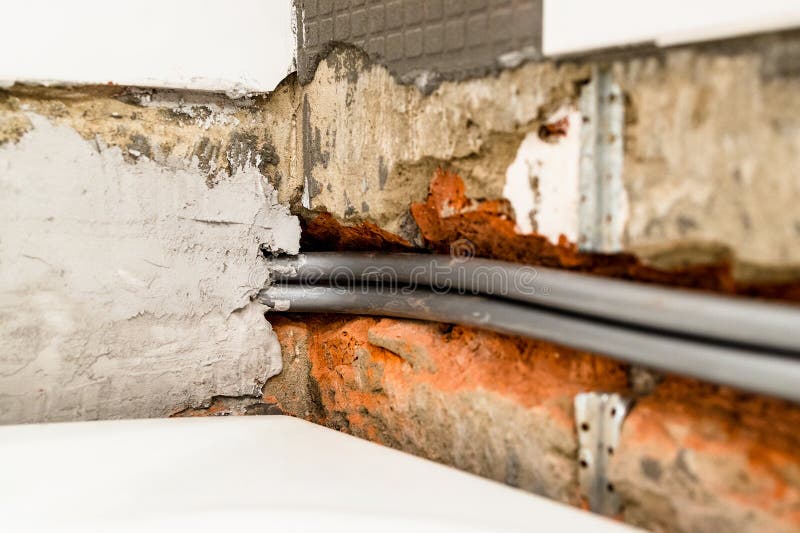 installation of new polyethylene flexible plumbing pipes in chiseled brick wall above white bathtub under removed ceramic tiles. installation of new polyethylene flexible plumbing pipes in chiseled brick wall above white bathtub under removed ceramic tiles