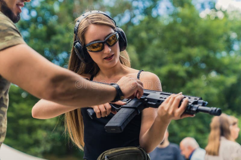 Instructeur utile explique comment utiliser un fusil à sa cliente célibataire caucasienne qui porte une protection image libre de droits