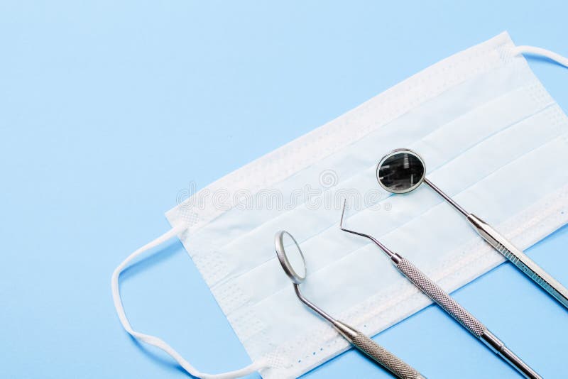 Instruments de dentiste : deux miroirs et gauche menteuse de sonde dentaire sur le masque médical sur le fond bleu-clair photo stock Instruments de dentiste : deux miroirs et gauche menteuse de sonde dentaire sur le masque médical sur le fond bleu-clair photo stock