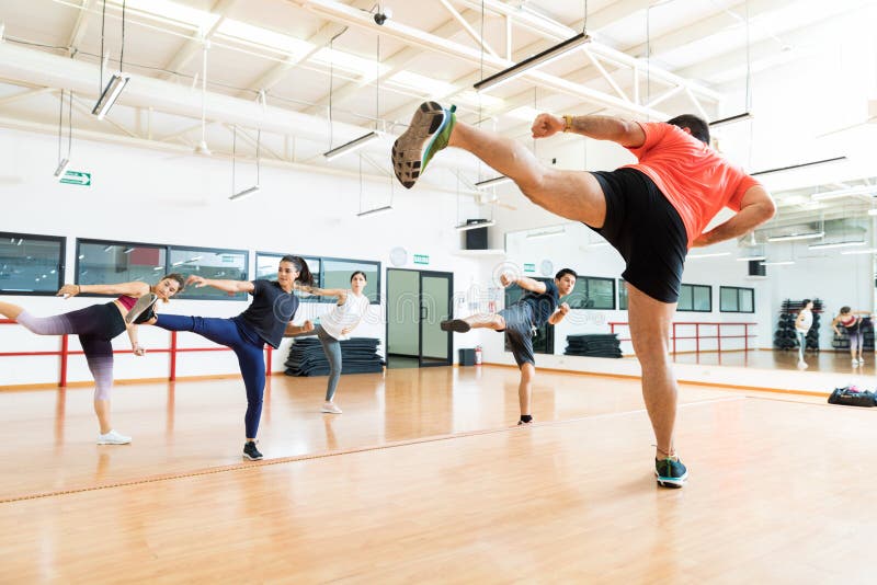 Full length of male instructor and clients kickboxing in dance class at gym. Full length of male instructor and clients kickboxing in dance class at gym