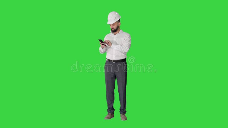 Intelligenter Ingenieur im weißen Hemd und Sicherheitstechnikhut mithilfe des Smartphone auf einem grünen Schirmfarbenreinheitssch stock video
