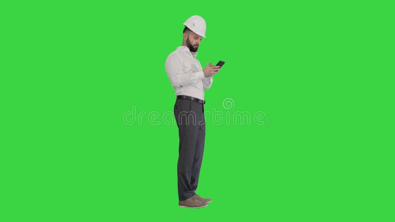 Intelligenter Ingenieur im weißen Hemd und Sicherheitstechnikhut mithilfe des Smartphone auf einem grünen Schirmfarbenreinheitssch stock video footage