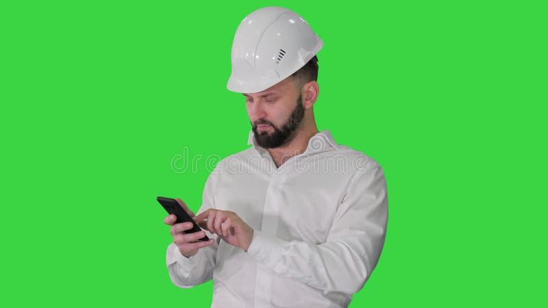 Intelligenter Ingenieur im weißen Hemd und Sicherheitstechnikhut mithilfe des Smartphone auf einem grünen Schirmfarbenreinheitssch stock video