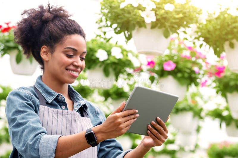 Intelligentes Gewächshaus mit digitaler Steuerung. Afrikanisches Mädchen mit Tablette in Händen stockfoto