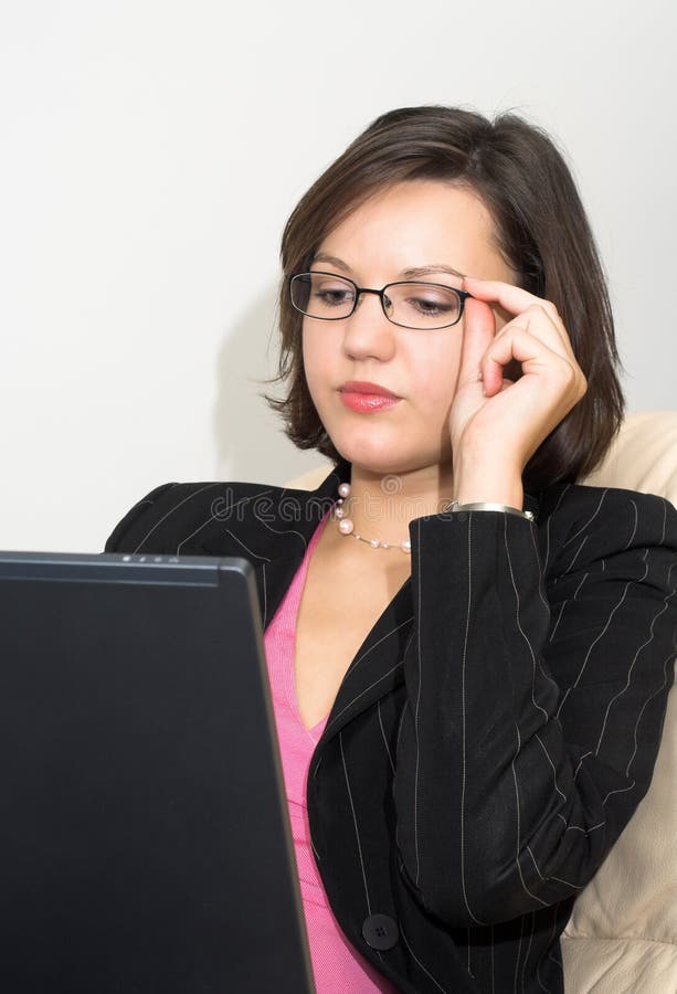 Young attractive business lady sitting on a sofa with laptop touches her glasses;. Young attractive business lady sitting on a sofa with laptop touches her glasses;