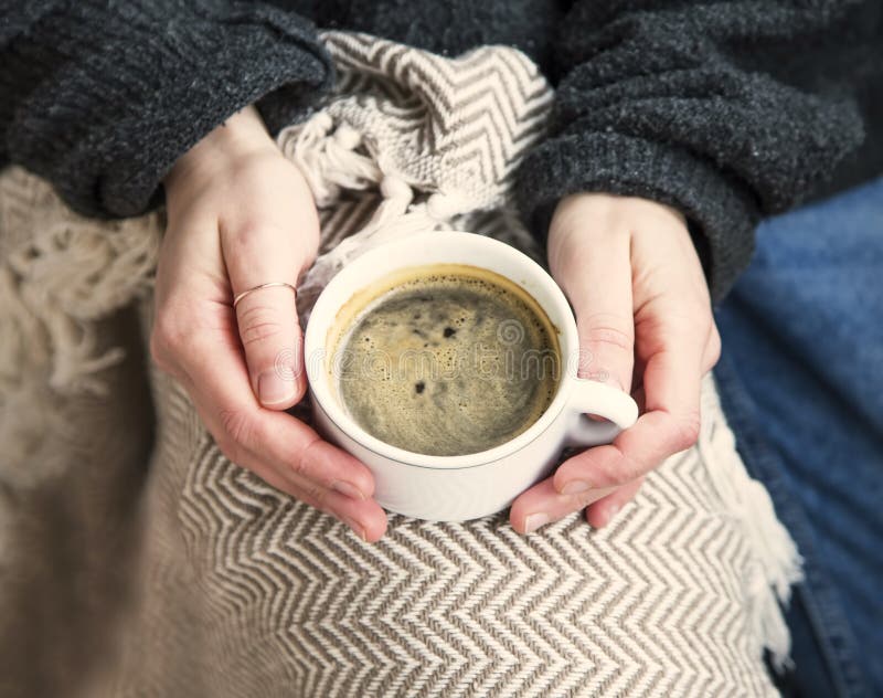 Interior cosy woman hands holding cup of coffee or chocolate with sweater and blanket, comfortable home winter or autumn lifestyle