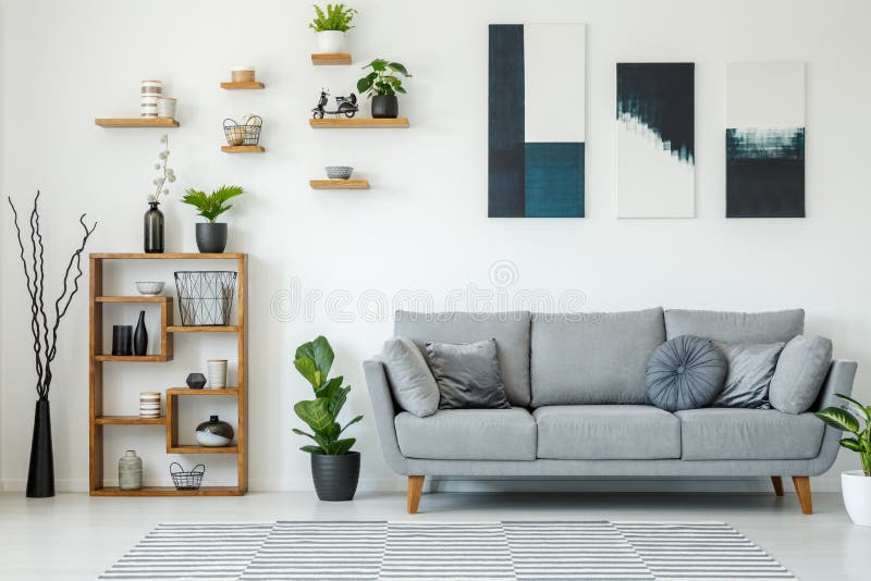 Interior elegante con un sofá gris, estantes de madera, p de la sala de estar imagen de archivo libre de regalías Interior elegante con un sofá gris, estantes de madera, p de la sala de estar imagen de archivo libre de regalías