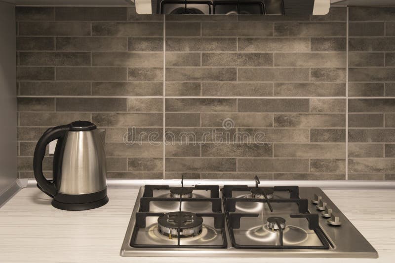 Interior of a modern kitchen. Close-up of electric kettle and gas hob on grey tile backsplash