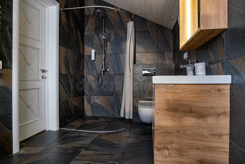 Interior of modern stylish bathroom with black tiled walls, curtain shower place and wooden furniture with wash basin and big