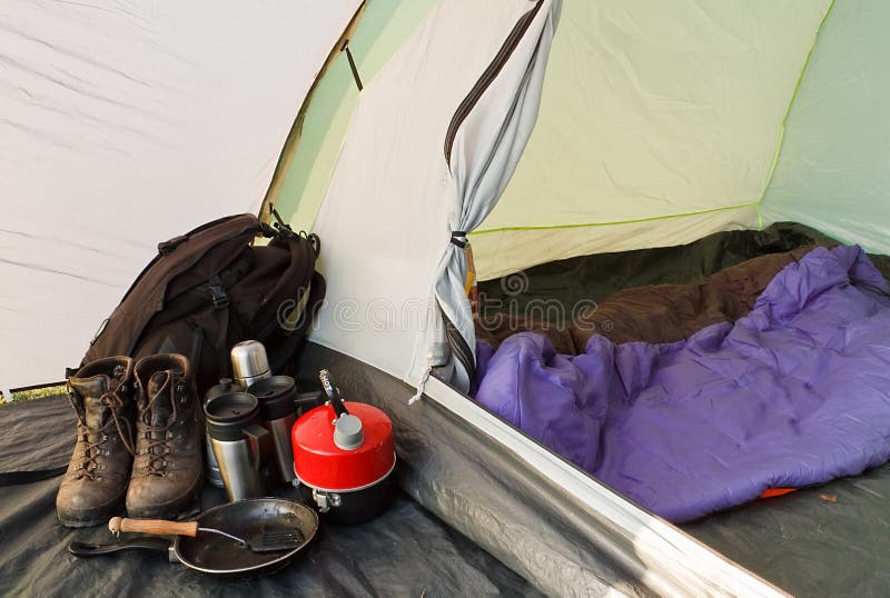 Interior view of a dome tent set up for camping with various equipment and sleeping bag inside inner compartment. Interior view of a dome tent set up for camping with various equipment and sleeping bag inside inner compartment