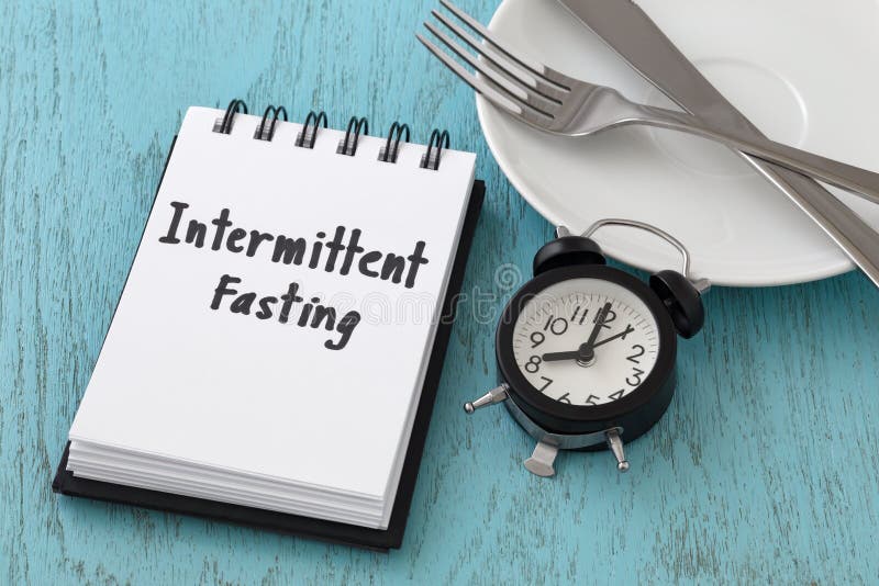 Intermittent fasting word on notepad with clock, fork and knife on white plate, intermittent fasting and weight loss concept. Intermittent fasting word on notepad with clock, fork and knife on white plate, intermittent fasting and weight loss concept
