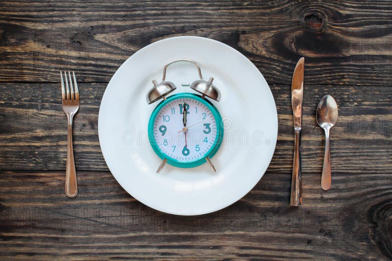 Twelve hour intermittent fasting time concept with clock on plate over a rustic wooden table / background. Top view. Twelve hour intermittent fasting time concept with clock on plate over a rustic wooden table / background. Top view