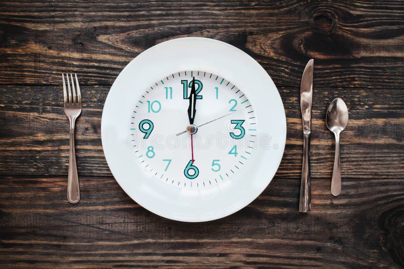 Twelve hour intermittent fasting time concept with clock on plate over a rustic wooden table / background. Top view. Twelve hour intermittent fasting time concept with clock on plate over a rustic wooden table / background. Top view