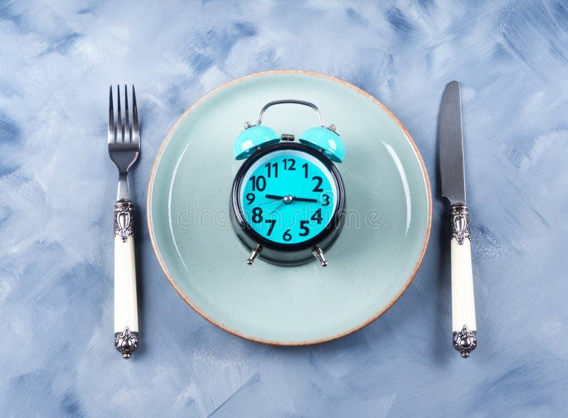 Intermittent fasting concept with blue alarm clock on empty dish with silverware. Intermittent fasting concept with blue alarm clock on empty dish with silverware