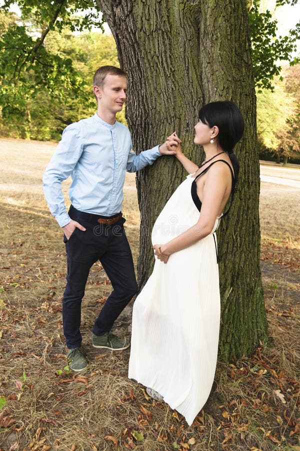 International family with pregnant woman standing near tree in park stock photography International family with pregnant woman standing near tree in park stock photography