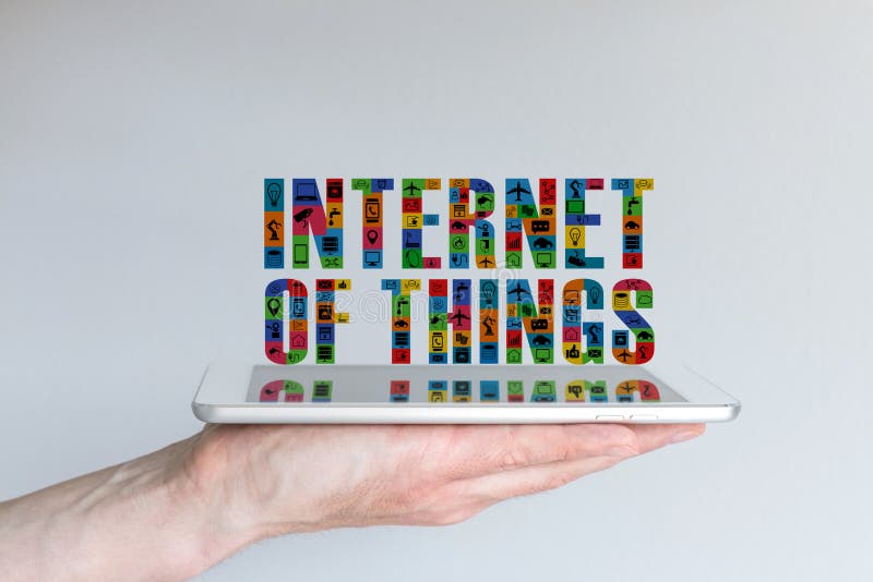 Internet of things (IoT) concept. Background with hand holding tablet and floating text in different colors and with symbols. Reflections on screen.