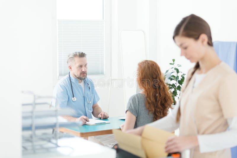 General practitioner in blue uniform with stethoscope during medical consultation with a patient. General practitioner in blue uniform with stethoscope during medical consultation with a patient