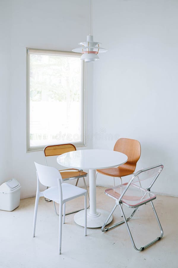 Portrait or vertical shot of minimalist and warm cafe interior contains plastic dining chair, a window, minimalist trash bin and 4 chairs with wooden, plastic, italian crystal classic, mini pendant. Portrait or vertical shot of minimalist and warm cafe interior contains plastic dining chair, a window, minimalist trash bin and 4 chairs with wooden, plastic, italian crystal classic, mini pendant