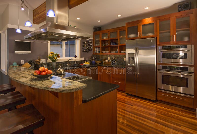 Interno domestico dell'alta società contemporaneo della cucina con i gabinetti e pavimenti di legno, controsoffitto del granito e