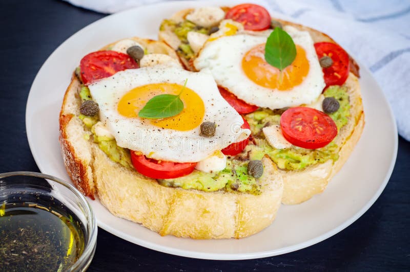 Interponga i pani tostati con agg, i pomodori ciliegia, la mozzarella, l'avocado, il basilico e l'olio d'oliva Vista laterale su fotografia stock Interponga i pani tostati con agg, i pomodori ciliegia, la mozzarella, l'avocado, il basilico e l'olio d'oliva Vista laterale su fotografia stock