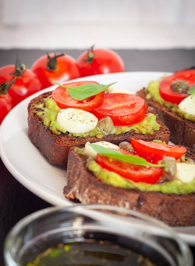 Interponga i pani tostati con i pomodori ciliegia, mozzarella, avocado, basilico e olio d'oliva Vista laterale su un piatto di pi fotografia stock Interponga i pani tostati con i pomodori ciliegia, mozzarella, avocado, basilico e olio d'oliva Vista laterale su un piatto di pi fotografia stock