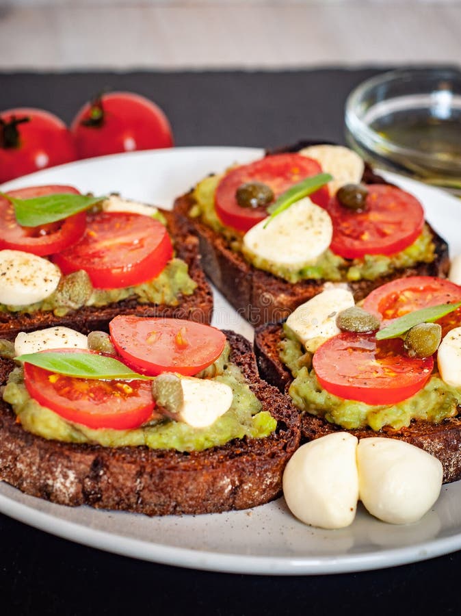 Interponga i pani tostati con i pomodori ciliegia, mozzarella, avocado, basilico e olio d'oliva Vista laterale su un piatto di pi immagine stock Interponga i pani tostati con i pomodori ciliegia, mozzarella, avocado, basilico e olio d'oliva Vista laterale su un piatto di pi immagine stock