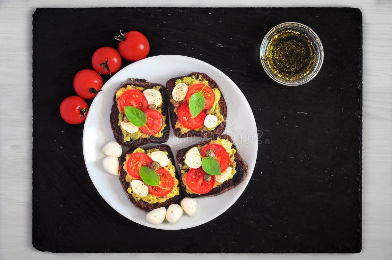 Interponga i pani tostati con i pomodori ciliegia, mozzarella, avocado, basilico e olio d'oliva Vista superiore su un piatto di p immagine stock libera da diritti Interponga i pani tostati con i pomodori ciliegia, mozzarella, avocado, basilico e olio d'oliva Vista superiore su un piatto di p immagine stock libera da diritti