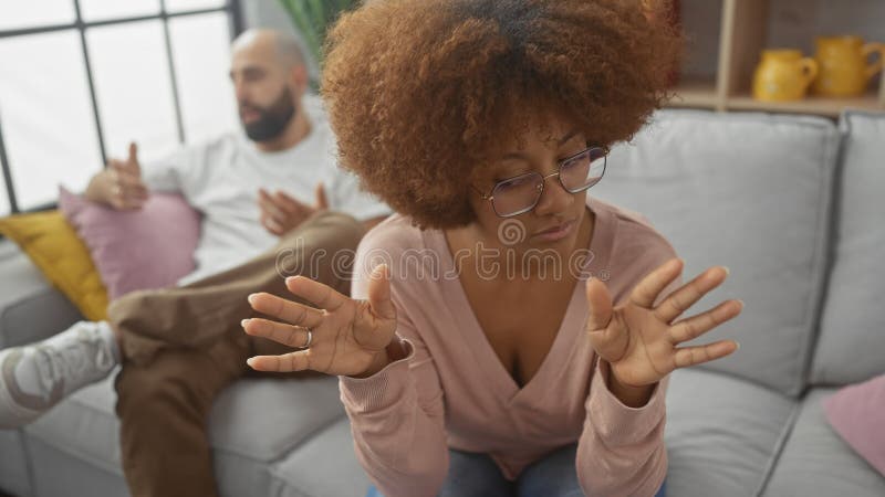 An interracial couple engages in a serious conversation in a modern living room, highlighting relationship dynamics stock photo