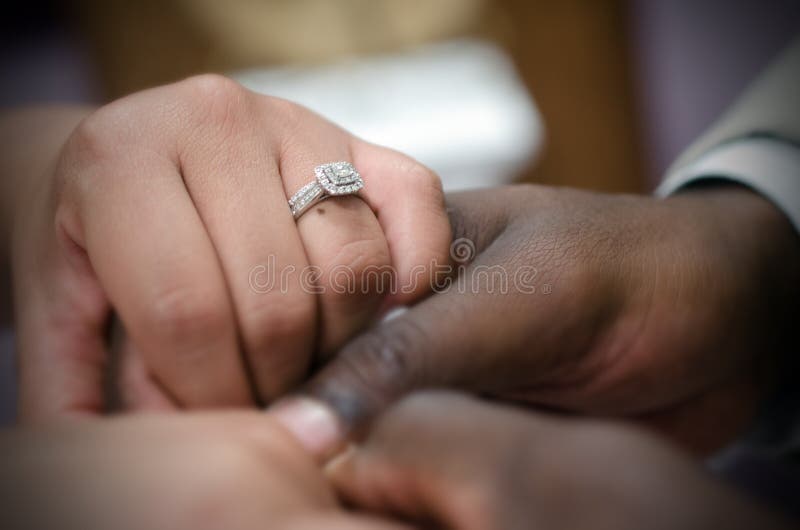 Interracial Hispanic bride and African American groom couple holding hands a the wedding altar repeating their vows. Silver and diamond wedding bands. Interracial Hispanic bride and African American groom couple holding hands a the wedding altar repeating their vows. Silver and diamond wedding bands.