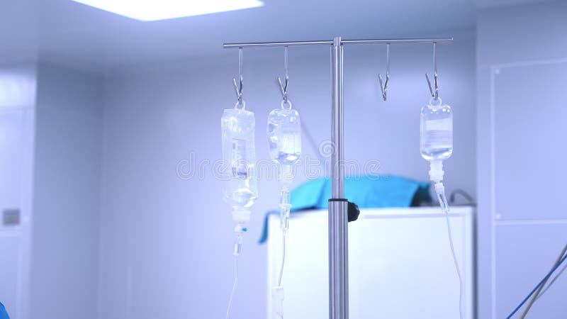 Intravenous drip in focus, surgical team performing surgery in background, out of focus