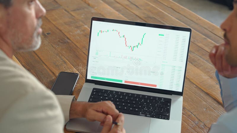 Inversor financiero explicando los datos del mercado de valores de inversión apuntando a una laptop.