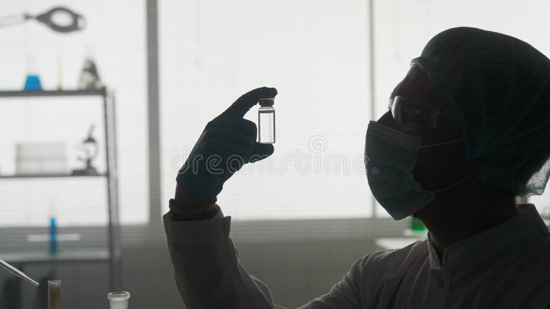 Investigación y desarrollo de una vacuna. silueta oscura de un científico masculino con un vial de ampolla de vidrio. concepto : e almacen de metraje de vídeo