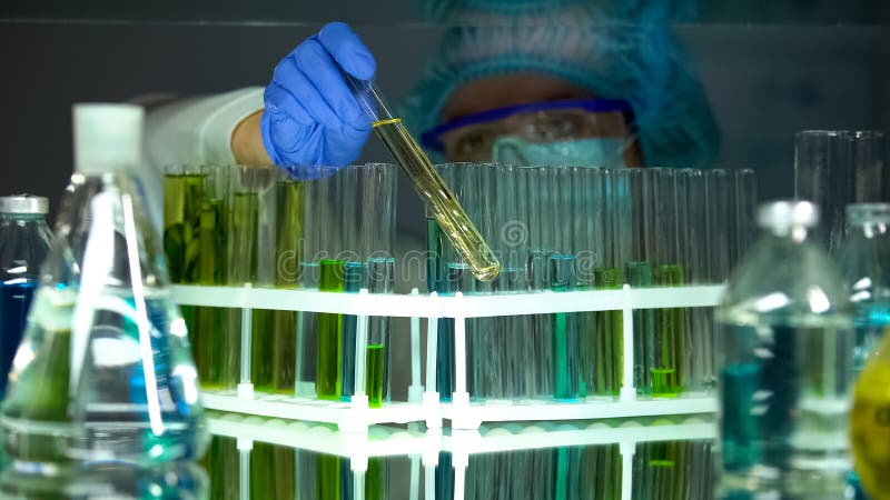 Investigador que comprueba los sedimentos en tubos con los l?quidos de la prueba, producci?n de la vitamina fotos de archivo Investigador que comprueba los sedimentos en tubos con los l?quidos de la prueba, producci?n de la vitamina fotos de archivo