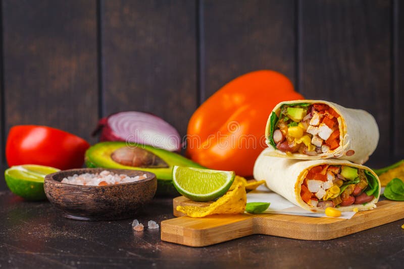 Involucri dei Burritos con il pollo, i fagioli, il mais, i pomodori e l'avocado sul bordo di legno, fondo scuro immagini stock libere da diritti Involucri dei Burritos con il pollo, i fagioli, il mais, i pomodori e l'avocado sul bordo di legno, fondo scuro immagini stock libere da diritti