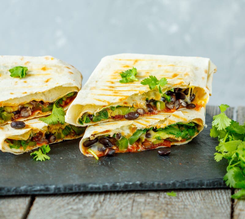 Involucri vegetariani dei burritos con i fagioli, l'avocado ed il formaggio su un'ardesia immagine stock libera da diritti Involucri vegetariani dei burritos con i fagioli, l'avocado ed il formaggio su un'ardesia immagine stock libera da diritti
