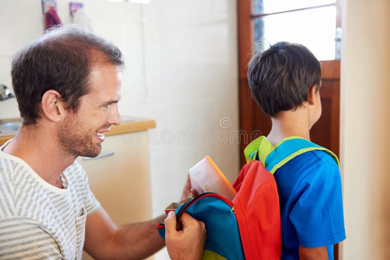 Father packing school lunch into son backpack before he goes to learn. Father packing school lunch into son backpack before he goes to learn