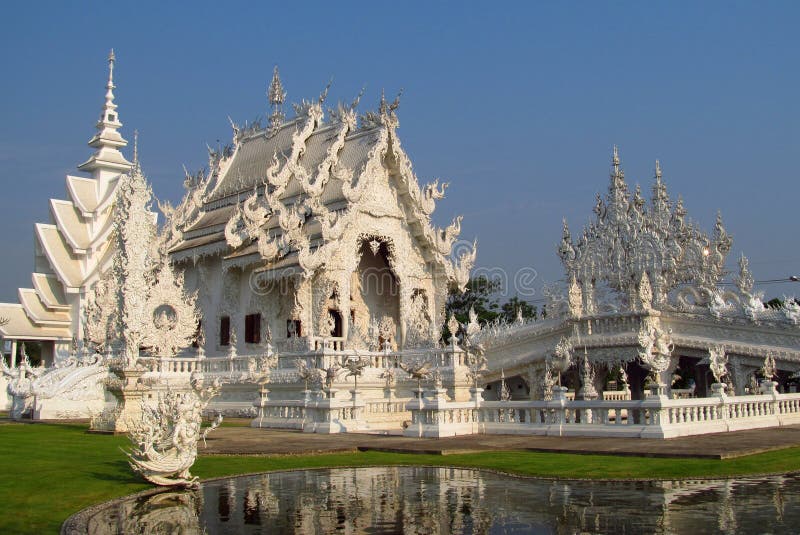 In blanc Chiang Rai de Wat Rong Khun de temple. In contemporain Chiang Rai Province,  Thaïlande de temple de Buddhist d'unconventional de Wat Rong Khun de temple blanc By conçu Chalermchai Kositpipat Belle pagoda avec les ornements blancs de sculptures, d'argent et de miroir Vue extérieure un jour ensoleillé avec le ciel bleu clair, l'herbe verte et les arbres et un lac devant le bâtiment de temple
