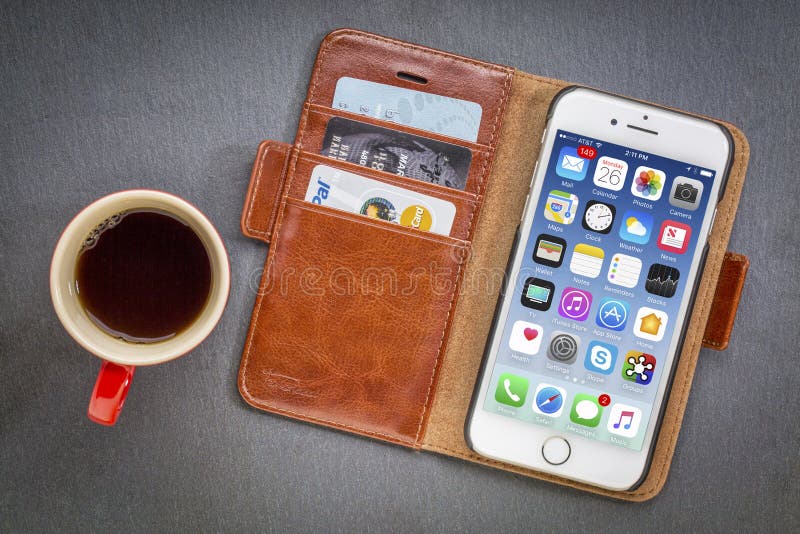 FORT COLLINS, CO, USA - JANUARY 1, 2017: iPhone 7 smart phone by Apple Computer Inc in a leather wallet with credit cards and coffee against stone background. FORT COLLINS, CO, USA - JANUARY 1, 2017: iPhone 7 smart phone by Apple Computer Inc in a leather wallet with credit cards and coffee against stone background.