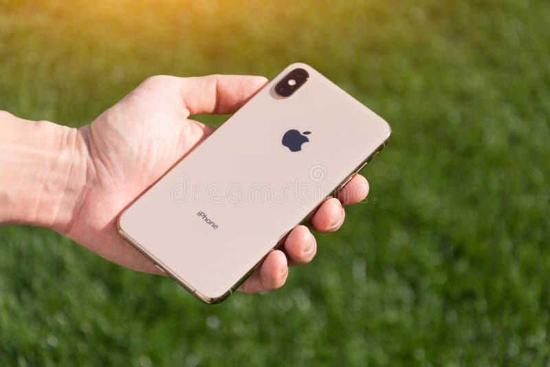 IPhone Xs Max gold smartphone model by Apple Computers close up in male hand on the background of green grass. Italy royalty free stock image IPhone Xs Max gold smartphone model by Apple Computers close up in male hand on the background of green grass. Italy royalty free stock image