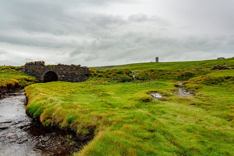 Irische Landschaftslandschaft mit einer alten Steinbrücke und dem Schloss Doonagore im Hintergrund lizenzfreie stockbilder Irische Landschaftslandschaft mit einer alten Steinbrücke und dem Schloss Doonagore im Hintergrund lizenzfreie stockbilder