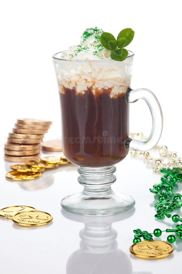 Mug of Irish Coffee with green sprinkles and clover leaf surrounded with gold coins and shamrock ornament for St Patrick's Day