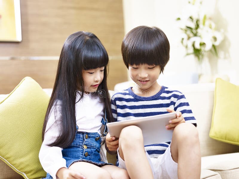 Little asian brother and sister sitting on couch using digital tablet together. Little asian brother and sister sitting on couch using digital tablet together.