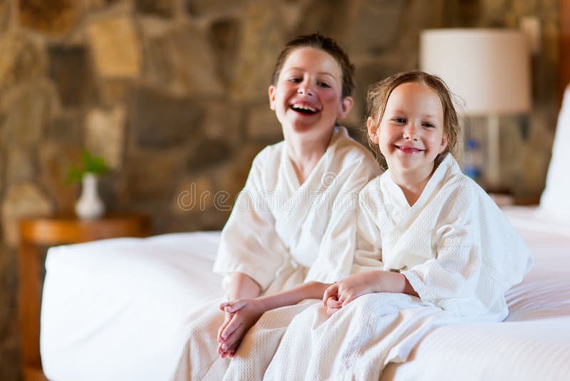 Two kids brother and sister wearing little bathrobes laughing while sitting on bed at hotel room or home. Two kids brother and sister wearing little bathrobes laughing while sitting on bed at hotel room or home