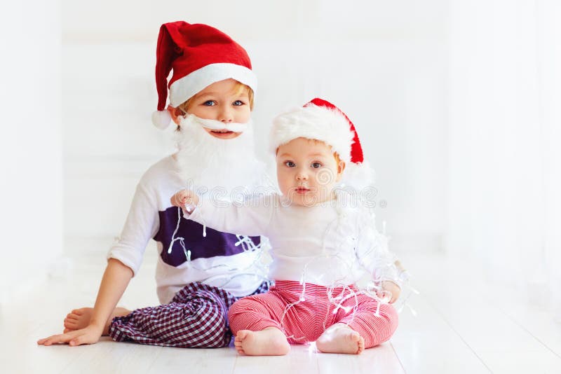 Irmãos bonitos do irmão, crianças em chapéus do ` s de Santa e festão que joga em casa fotografia de stock Irmãos bonitos do irmão, crianças em chapéus do ` s de Santa e festão que joga em casa fotografia de stock