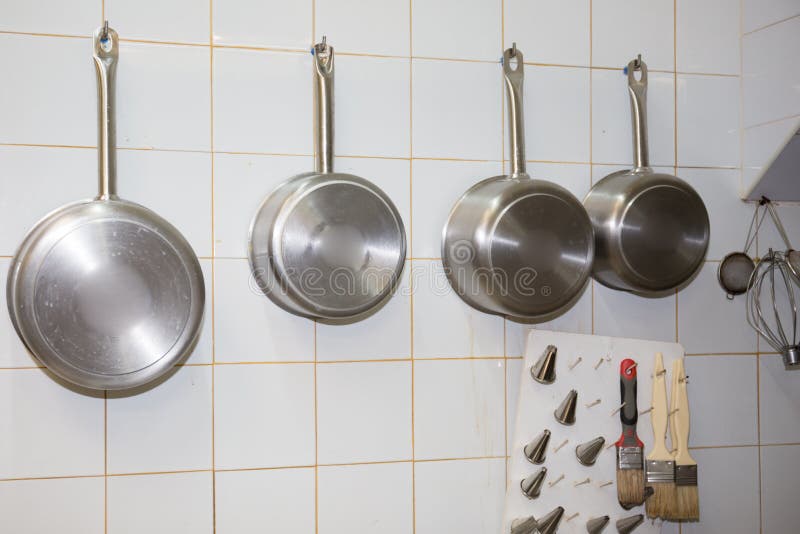 Iron Frying Pan and Utensils Hanging on the Wall in Bakery Room Stock