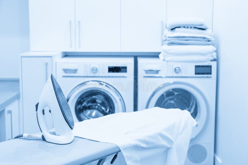 Iron on Ironing Board with White Shirt in Laundry Room Stock Photo