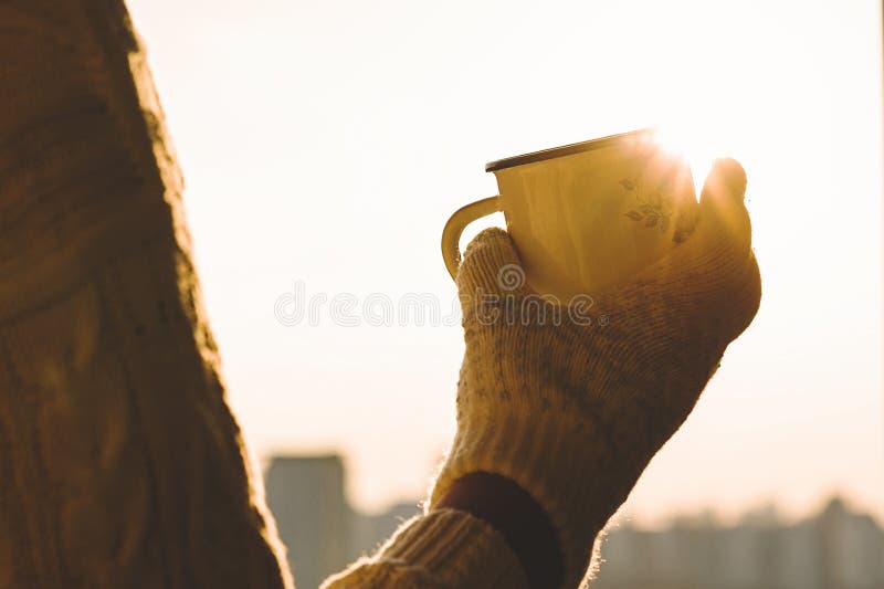 Iron mug with hot tea in female hands in knitted mittens on a winter frosty day against sunset sky