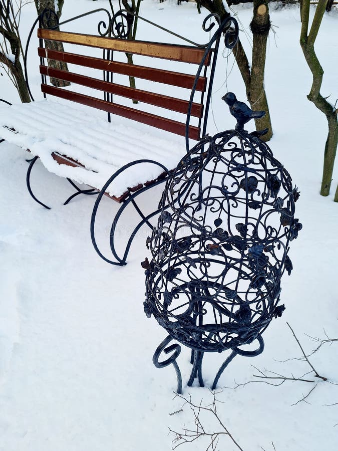 Iron Openwork Cage with a Bird on Top and a Snowcovered Bench in the