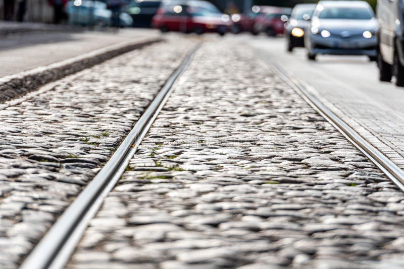 The iron rails for the tram on a cobblestone paved street, blurred traffic in background. Cobblestone street with tram rail tracks in Riga, Latvia, blurred traffic in background